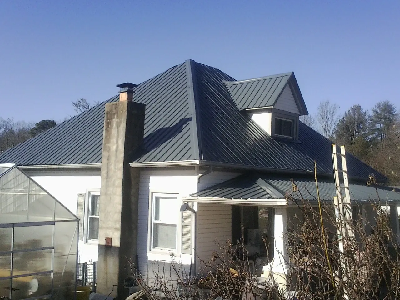 Dark blue standing seam metal roof on a white farmhouse with dormer — Slate & Tile Roof Repair by Roofing Brothers in Punta Gorda