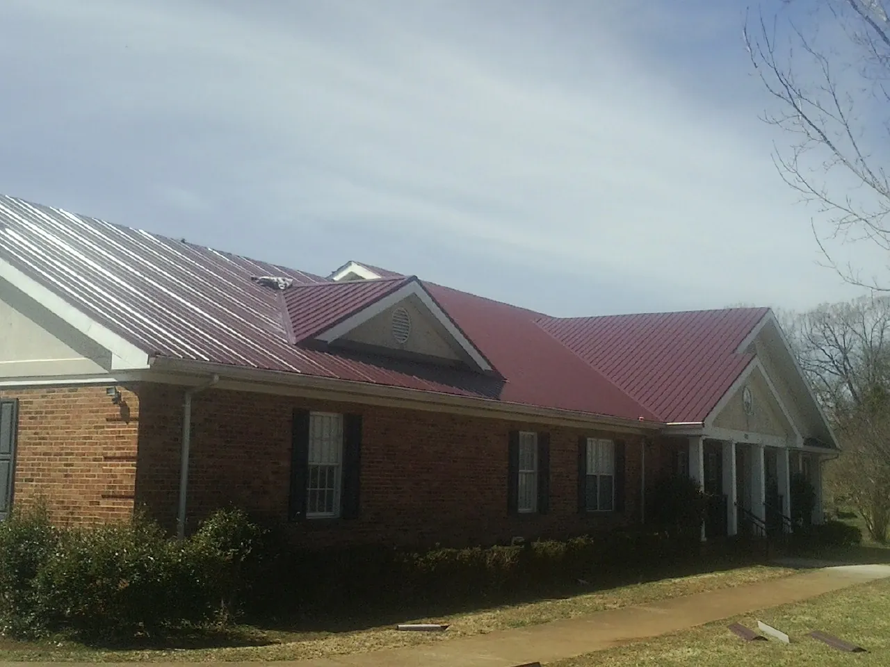 Red metal roof with gabled entries on a long brick building, from a Hail Damage Roof Repair job in Punta Gorda
