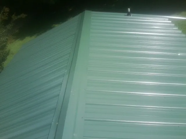 New green metal panels meeting at the ridge of a roof — Flat Roof Repair work by our crew in Punta Gorda