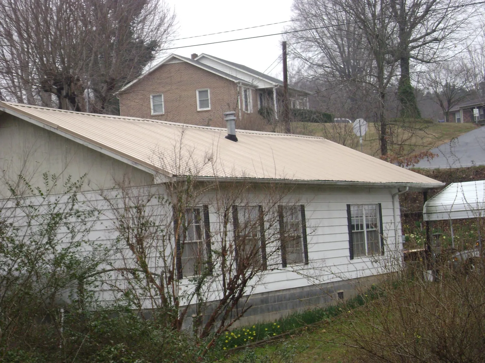 Tan metal roof on a white sided house set into a hillside — Commercial Roofing by Roofing Brothers in Punta Gorda